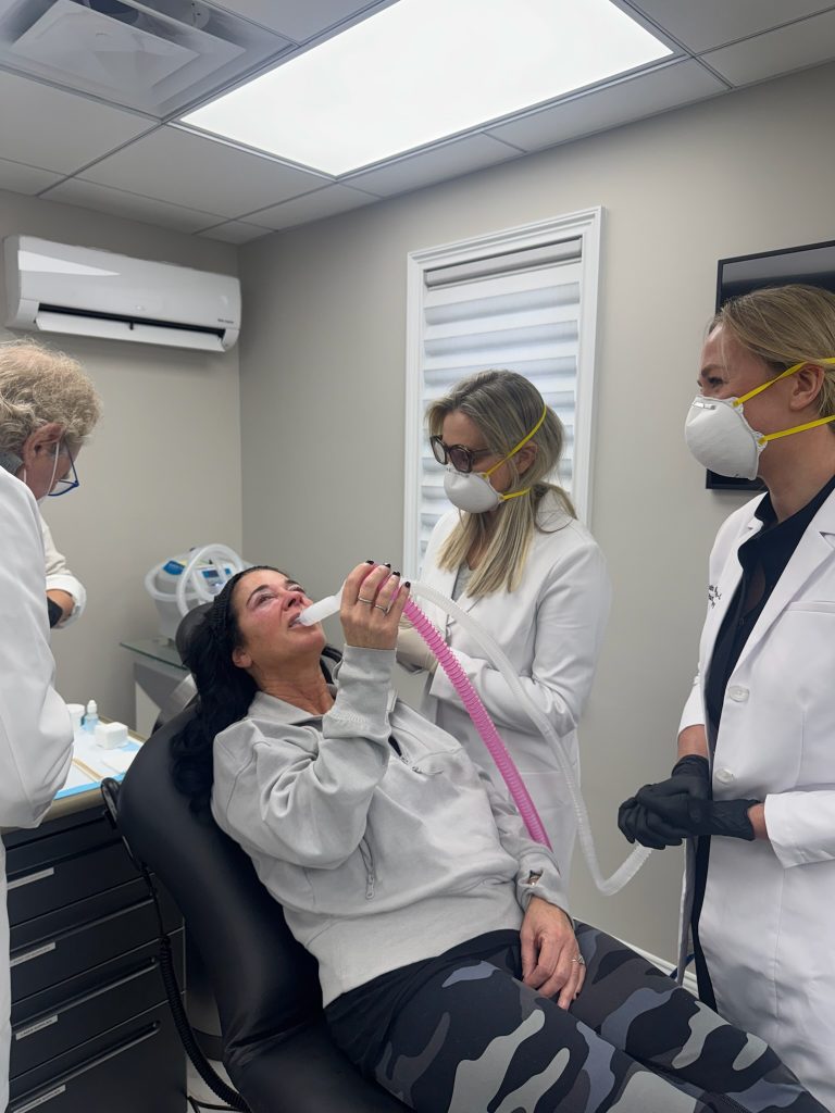 A patient uses a hose to direct cool air at her skin to relieve discomfort during a croton oil peel.